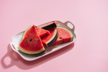 Fresh sliced watermelon in white dish on pink background.