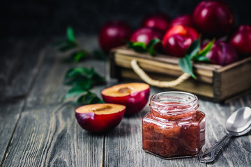 Homemade cinnamon plum jam in glass jar on rustic wooden background. Selective focus, space for...