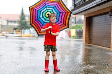 Kid boy wearing red rain boots and walking with umbrella