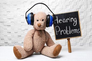 Toy bear, headphones and chalkboard with words HEARING PROBLEMS on table