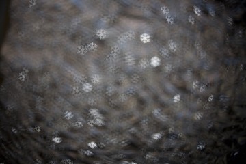 Sparkling spots of figured Bokeh - shining white snowflakes, water surface is not in focus, the background, metal, blue tint
