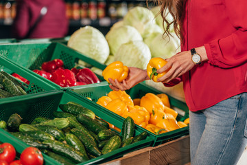Partial view of shopper choosing fresh raw bell peppers in hypermarket