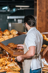 back view of male shop assistant arranging fresh bread in supermarket