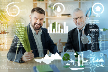 Super idea. Cheerful emotional professional engineers sitting at the table with miniature objects in front of them and putting their thumbs up while smiling happily
