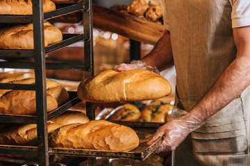 cropped shot of shop assistant arranging loafs of bread in supermarket
