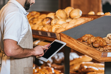 cropped shot of shop assistant in apron using tablet with blank screen in supermarket