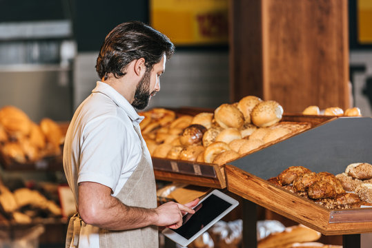 side view of shop assistant in apron using tablet with blank screen in supermarket - Powered by Adobe