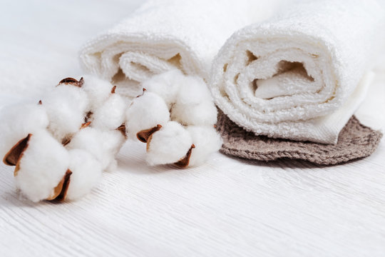 Spa composition. Two white  fluffy towels  and cotton flowers on light wooden background with copy space.