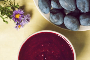 Fresh tkemali Georgian sauce from plums. A plate of sauce, a plate with plums, and flowers. top view.