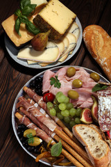 Italian antipasti wine snacks set. Cheese variety, Mediterranean olives, pickles, Prosciutto di Parma, salami and wine in glasses over black grunge background.