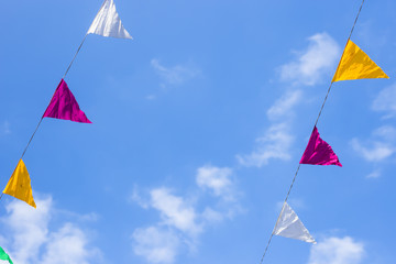 Multi-colored flags decoration hanging on a background of blue sky with white clouds. Copyspace