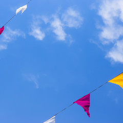 Multi-colored flags decoration hanging on a background of blue sky with white clouds. Copyspace