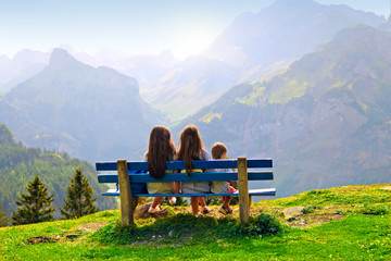 family sitting on a bench in nature and looking at the view of a mountain landscape, the sky and beautiful panorama