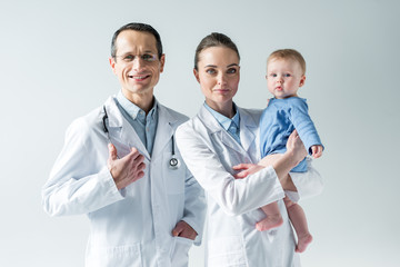 happy adult pediatricians with little baby on grey