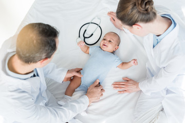 Obraz premium high angle view of pediatricians playing with little baby on bed