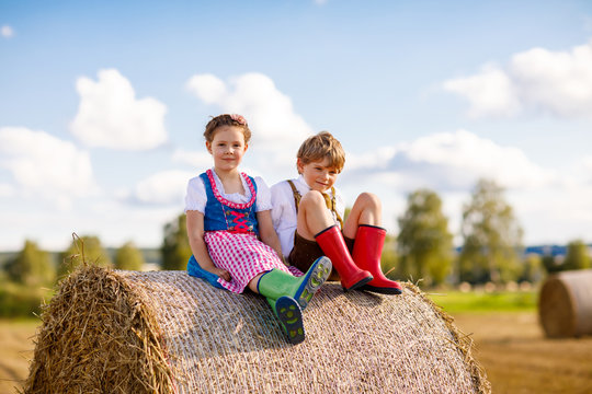 Adorable little kid boy and girl in traditional Bavarian costumes in wheat field on hay stack