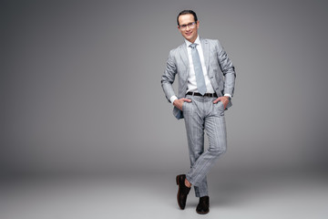 handsome adult businessman in stylish suit with hands in pockets on grey