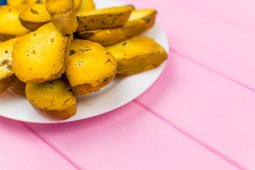 Rusks on a white plate on a pink wooden background.