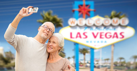 Fototapeta na wymiar vacation, tourism and travel concept - happy senior couple hugging and taking photo by digital camera over welcome to fabulous las vegas sign background