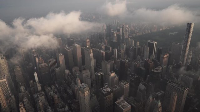 New York City aerial view flying over Midtown Manhattan skyscrapers toward Central Park, under fog and low level clouds at sunrise.