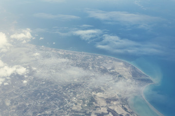 Obraz premium Top view from landing airplane. Window plane with copy space. Aerial view of cloud, sea, ocean and city landscape