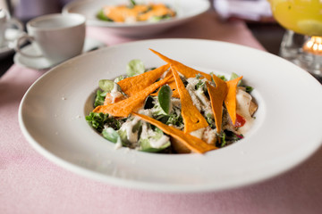 Caesar salad with chicken, greens and crispy chips on the table. Business lunch with a beautiful pineapple-orange tea in a glass teapot.