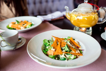 Caesar salad with chicken, greens and crispy chips on the table. Business lunch with a beautiful pineapple-orange tea in a glass teapot.
