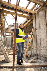 Naklejka na ściany i meble Man in hardhat and green jacket posing on building site