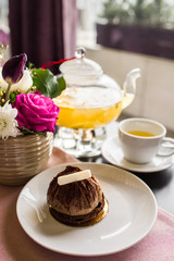 Chocolate truffle cake dessert with white chocolate. Pineapple tea with a transparent glass teapot. Citrus vitamin tea and a beautiful bouquet of flowers with roses, daisies and tulips on the table.