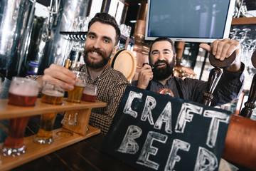 Happy bearded men test beer of different styles in beer samplers in brewery of craft beer.