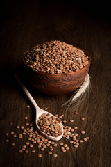 Lentil in a wooden bowl on a wooden background near the ears of wheat. wooden spoon with Lentil