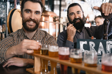 Two bearded men test beer of different styles in beer samplers in brewery of craft beer.