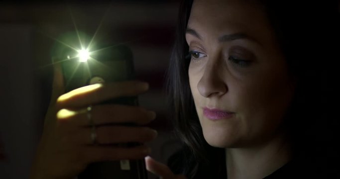 BCU young woman using cellphone at night, turns from screen with serious look on her face. Hand-held 4K with lens flares. Stripes of flag faintly visible behind.