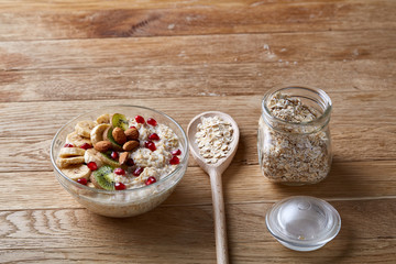 Composition with bowl of oatmeal porrige and dry oatmeal in glassware on wooden table indoors