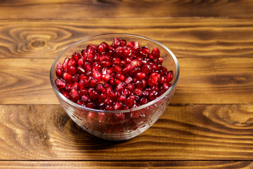 Pomegranate seeds in glass bowl on wooden table