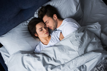 Bearded man embracing attractive brunette woman while sleeping in bed