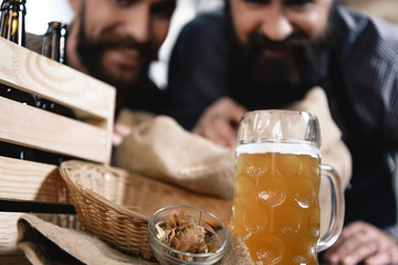In foreground of men is glass of freshly brewed beer and bowl of cones of hops.