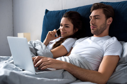 Young man and woman using digital devices while lying in bed