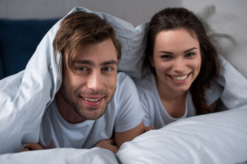 Smiling man and woman lying in bed under blanket