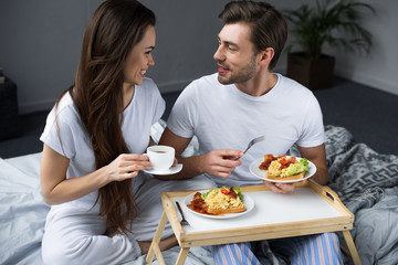 Beautiful young couple drinking coffee and eating breakfast in bed