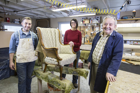 Senior Caucasian man upholsterer and his understudy team of young people working on an antique chair.