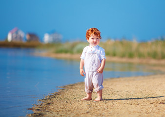 cute redhead toddler baby boy walking at lake coast in the summer morning