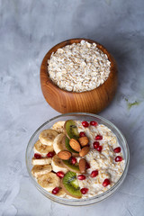 Diet breakfast oatmeal with fruits and bowl with oat flakes, selective focus, close-up, vertical
