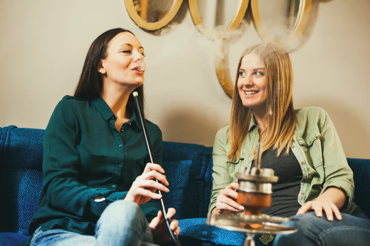 Two happy women are sitting in shisha bar and smoking nargile 
