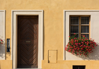 Fototapeta na wymiar The yellow facade of the old houses. Entrance wooden door and window with flowers