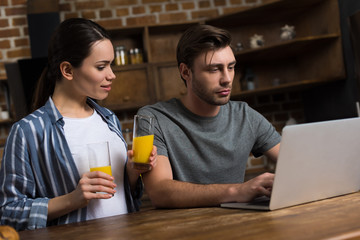 Wife offering juice to her husband working at laptop