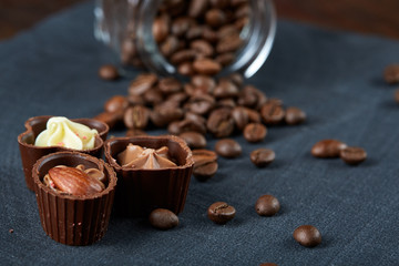 Side view of overturned glass jar with coffee beans and chocolate candies on wooden background, selective focus