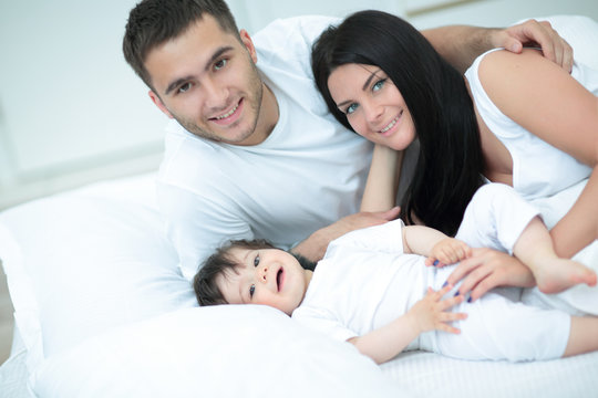 Smiling mother and father with their baby son hugging in bed