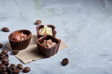Sweet chocolate candies with coffee beans over white textured background, selective focus, close-up.