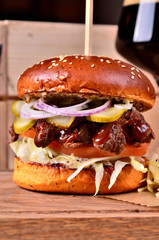Fresh homemade hamburger with beef, onion, sause and cabbage garnish on a wooden board, wooden table background. Juicey gourmet burger, fast food concept.